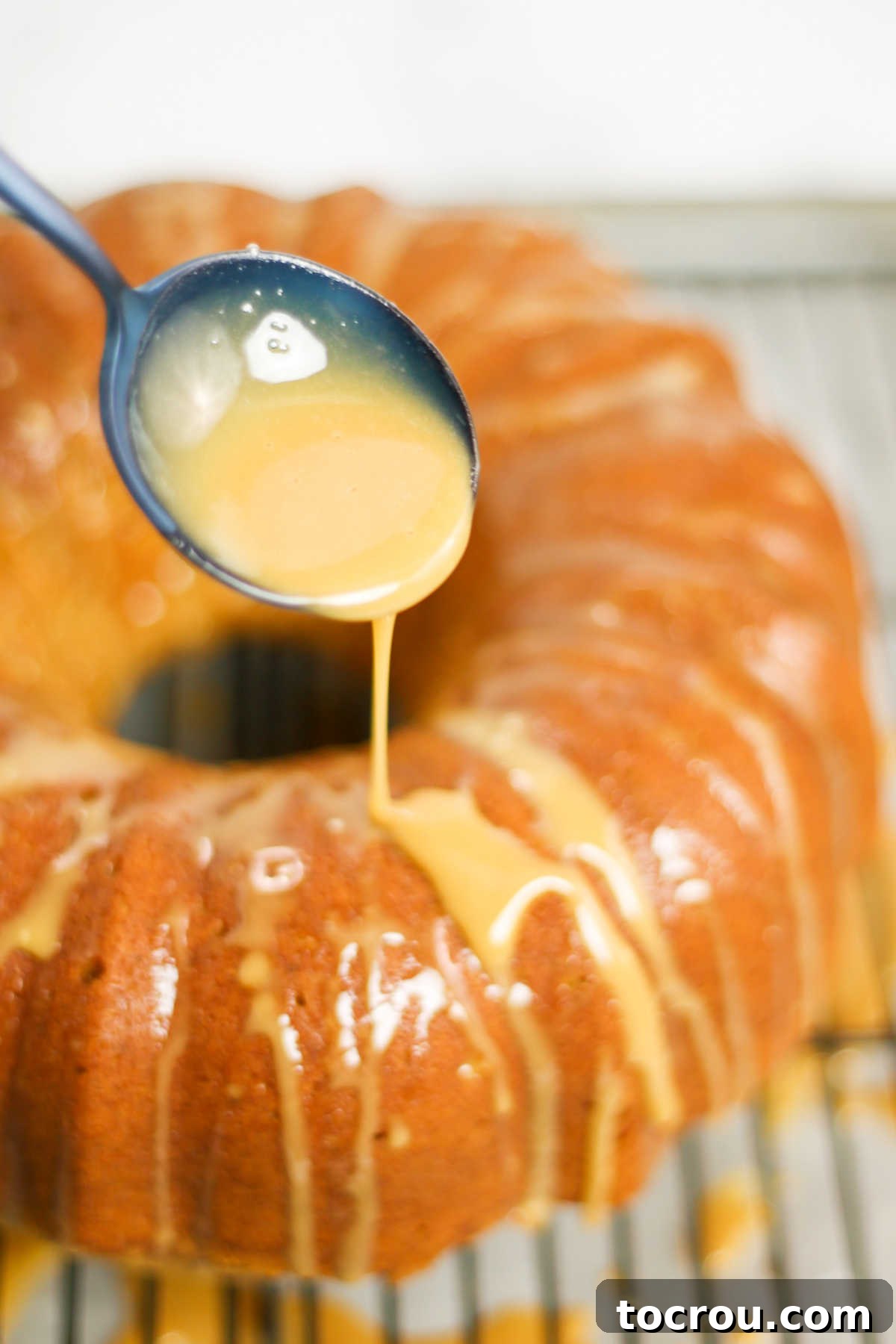 A spoon delicately drizzling rich espresso glaze over the warm, spiced surface of a freshly baked chai bundt cake, creating a beautiful finish.