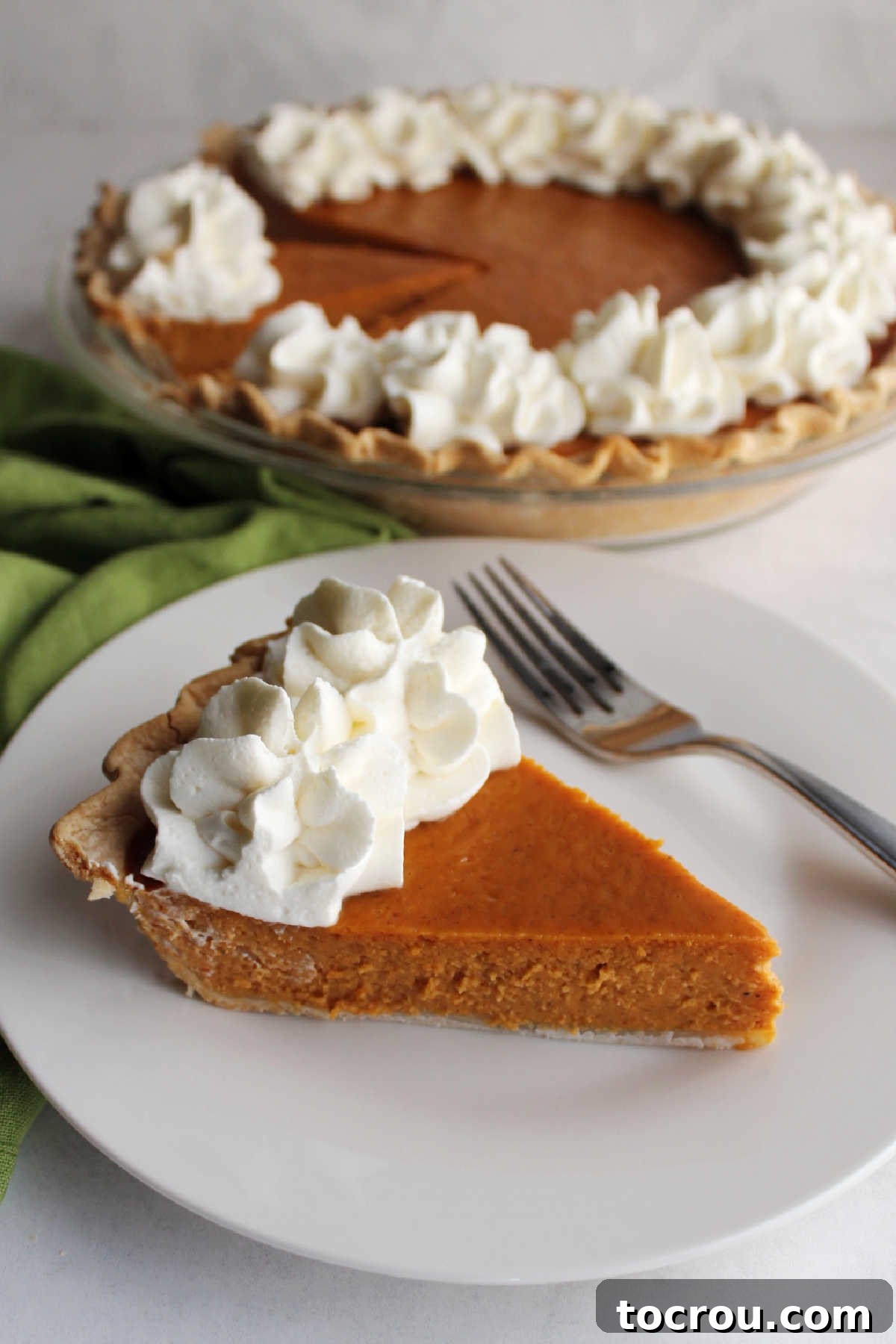 The Ultimate Pumpkin Pie Slice with Whipped Cream A delectable slice of pumpkin pie, impeccably presented on a plate and topped with a generous swirl of whipped cream, a fork poised nearby, inviting you to indulge.