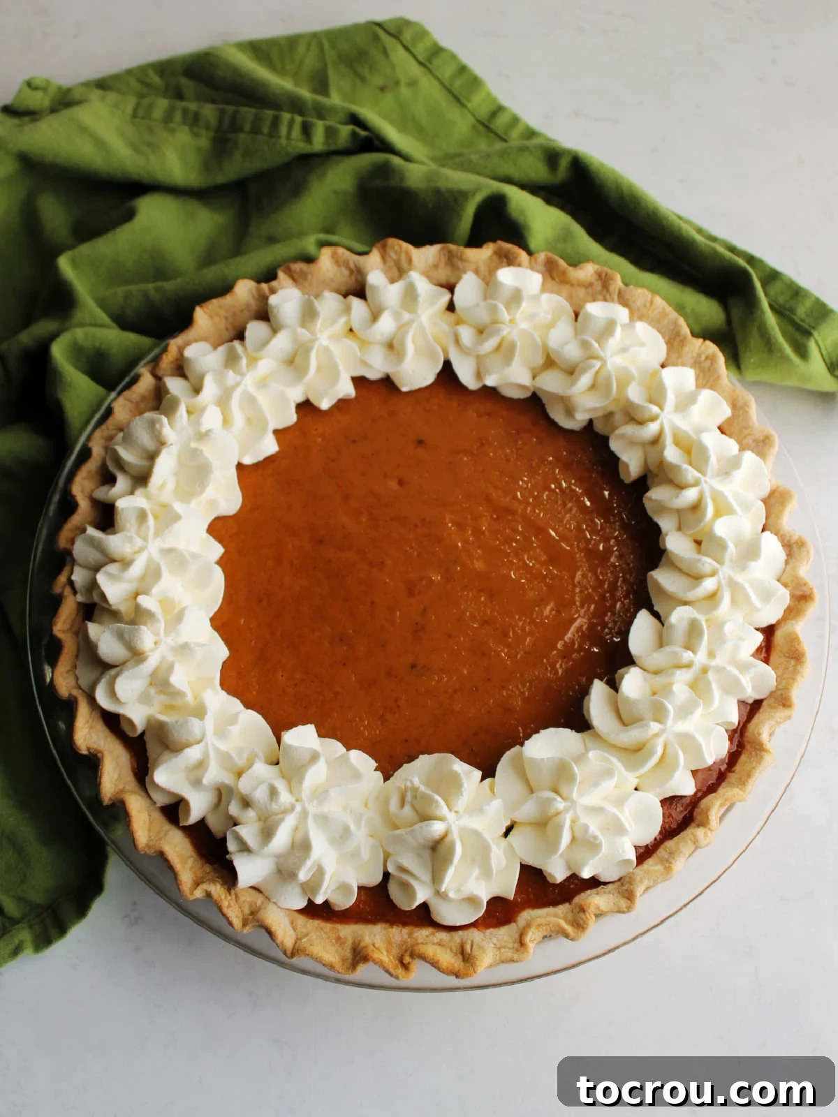Baked to Perfection: Pumpkin Pie with Cream Cheese Whipped Cream A beautifully baked and cooled pumpkin pie, its condensed milk filling set to perfection, adorned with ruffly dollops of cream cheese whipped cream piped elegantly around the edge, awaiting its first slice.