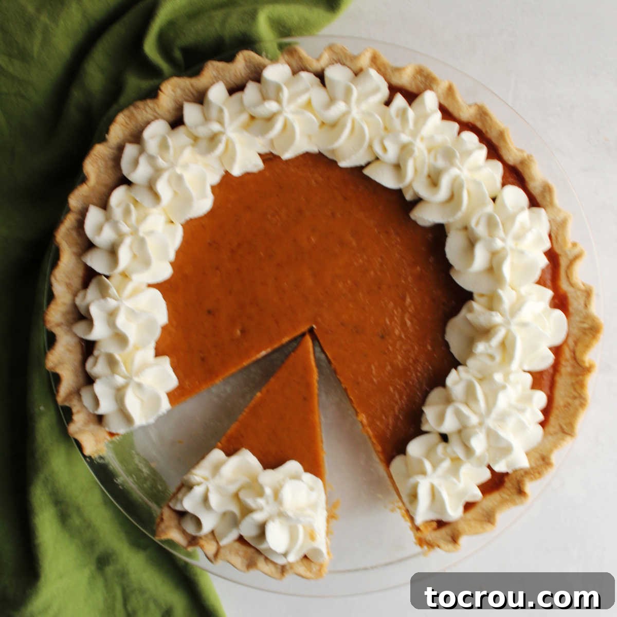 Pumpkin Pie Ready for Serving with Whipped Cream Border A visually appealing condensed milk pumpkin pie, beautifully adorned with piped cream cheese whipped cream around its border, with one satisfying slice already removed.