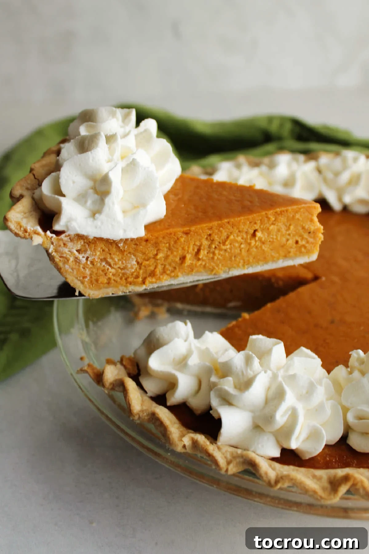 The Perfect Slice: Smooth Pumpkin Pie Filling A moment captured: lifting a perfect slice of pumpkin pie from the whole, revealing its smooth, custardy filling and a generous dollop of whipped cream topping.