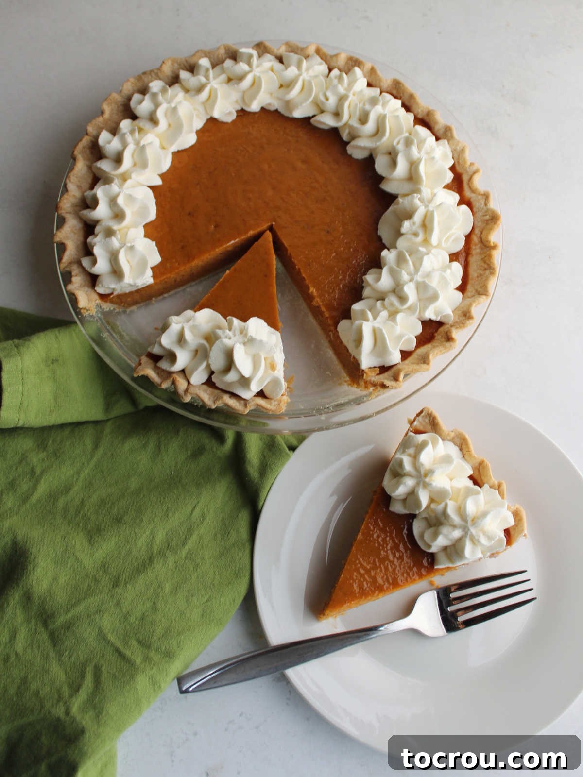 Ready to Enjoy: A Slice of Homemade Pumpkin Pie A delightful slice of pumpkin pie, elegantly presented on a dessert plate with a fork, adorned with creamy whipped cream, alongside the remainder of the pie.