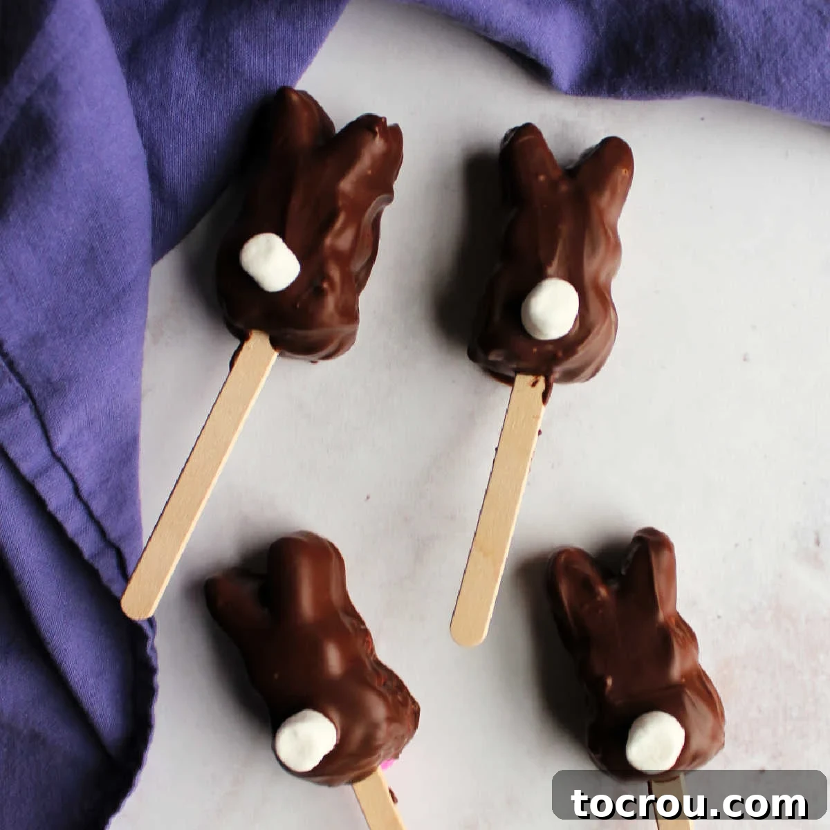 Chocolate dipped marshmallow bunnies with popsicle sticks and marshmallow tails.