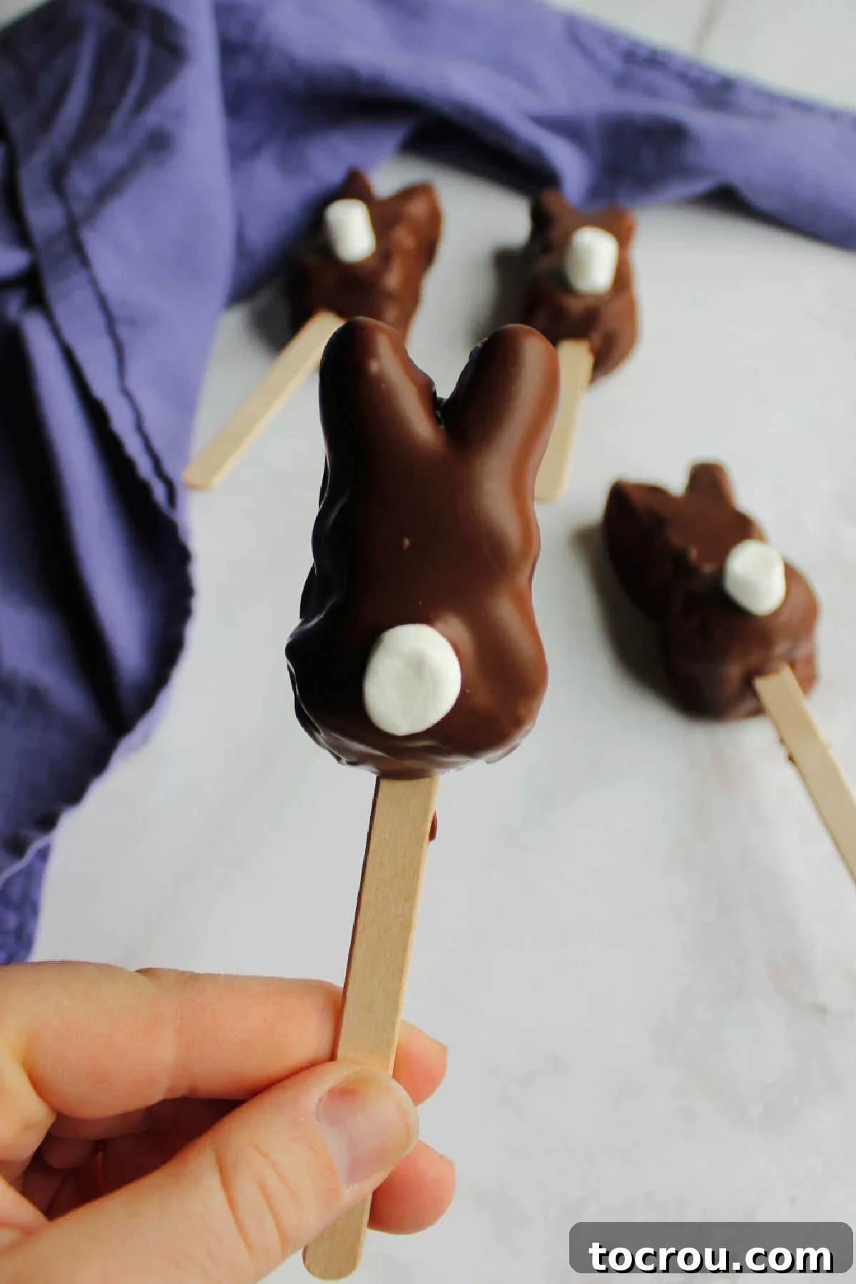 Hand holding popsicle stick with chocolate dipped peep bunny with white fluffy tail.