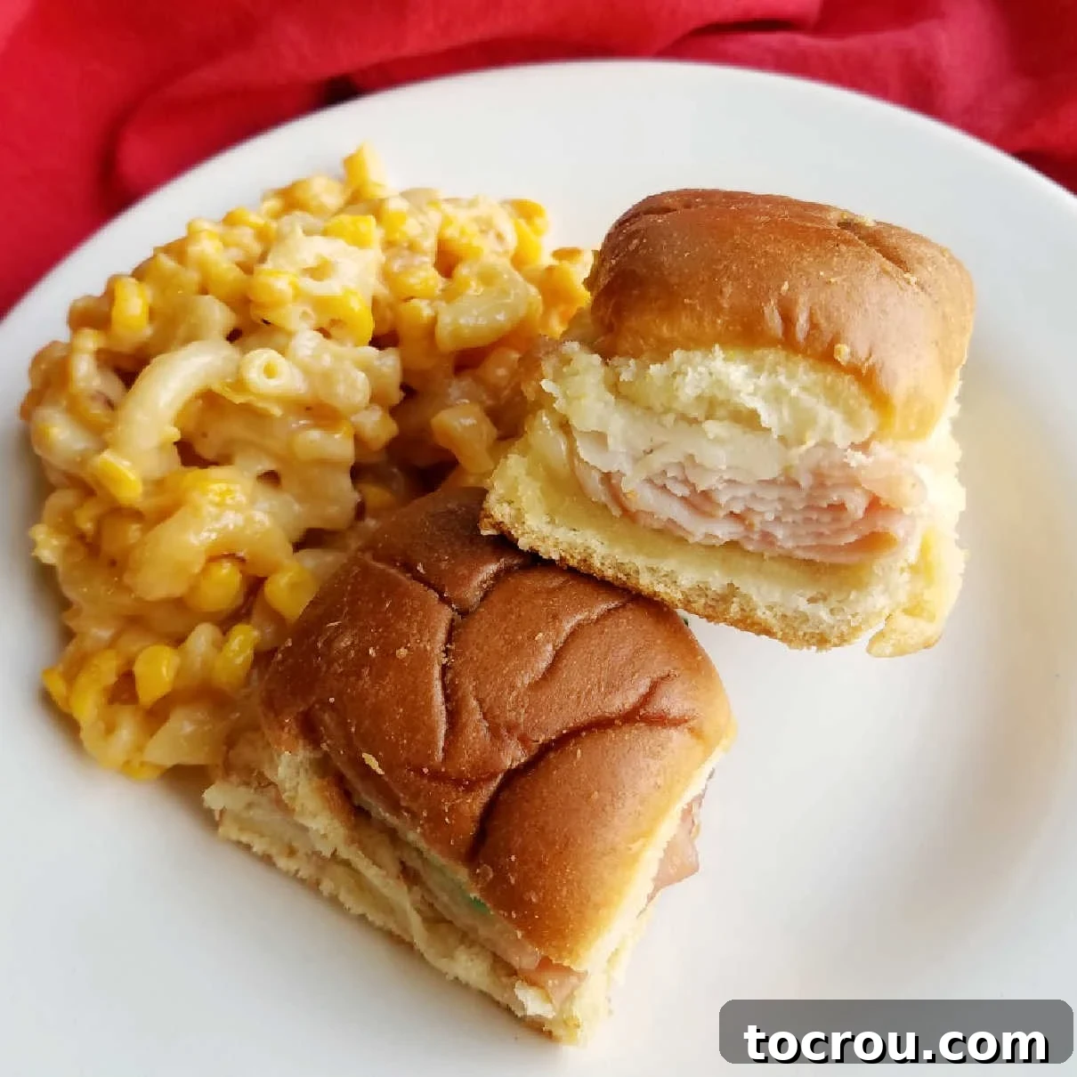 Delicious turkey, ham, and cheese sliders on a plate with macaroni and cheese and corn, perfect for any occasion.