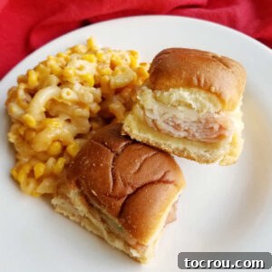 A plate of golden-brown turkey ham and cheese sliders, served with macaroni and cheese and corn.