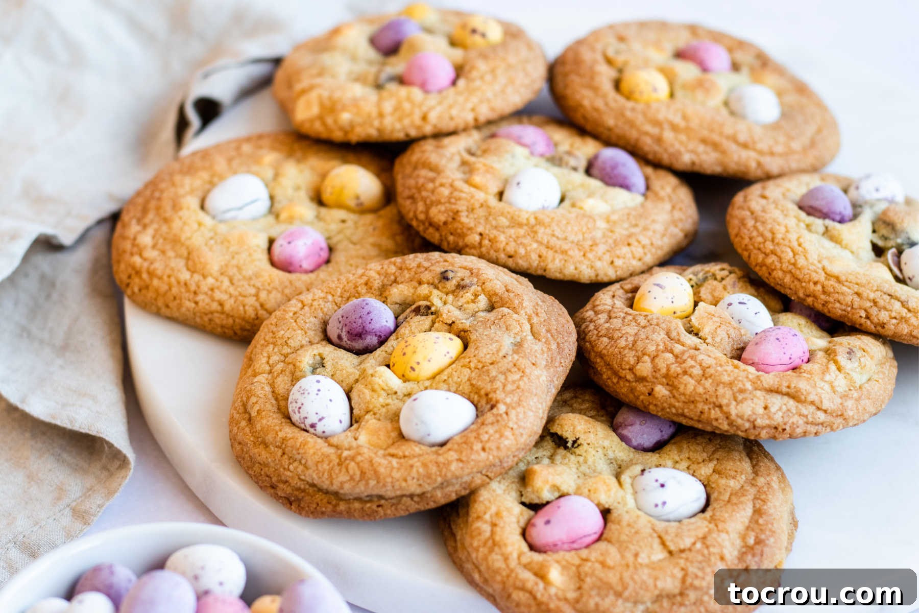Chewy cookies with pastel mini Cadbury egg chocolate baked inside and pushed into the top, ready to eat, served on a rustic wooden board.