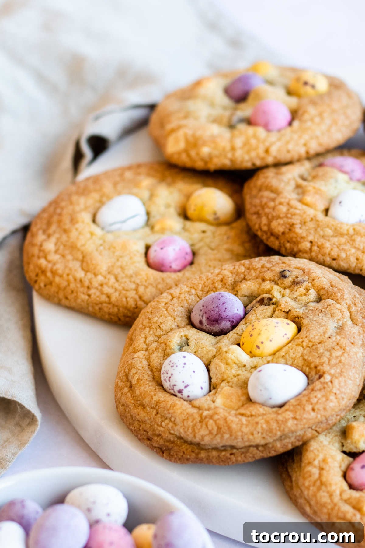 Close up of freshly baked, golden brown cookies with vibrant mini chocolate eggs visible on top, showcasing a delightful texture.