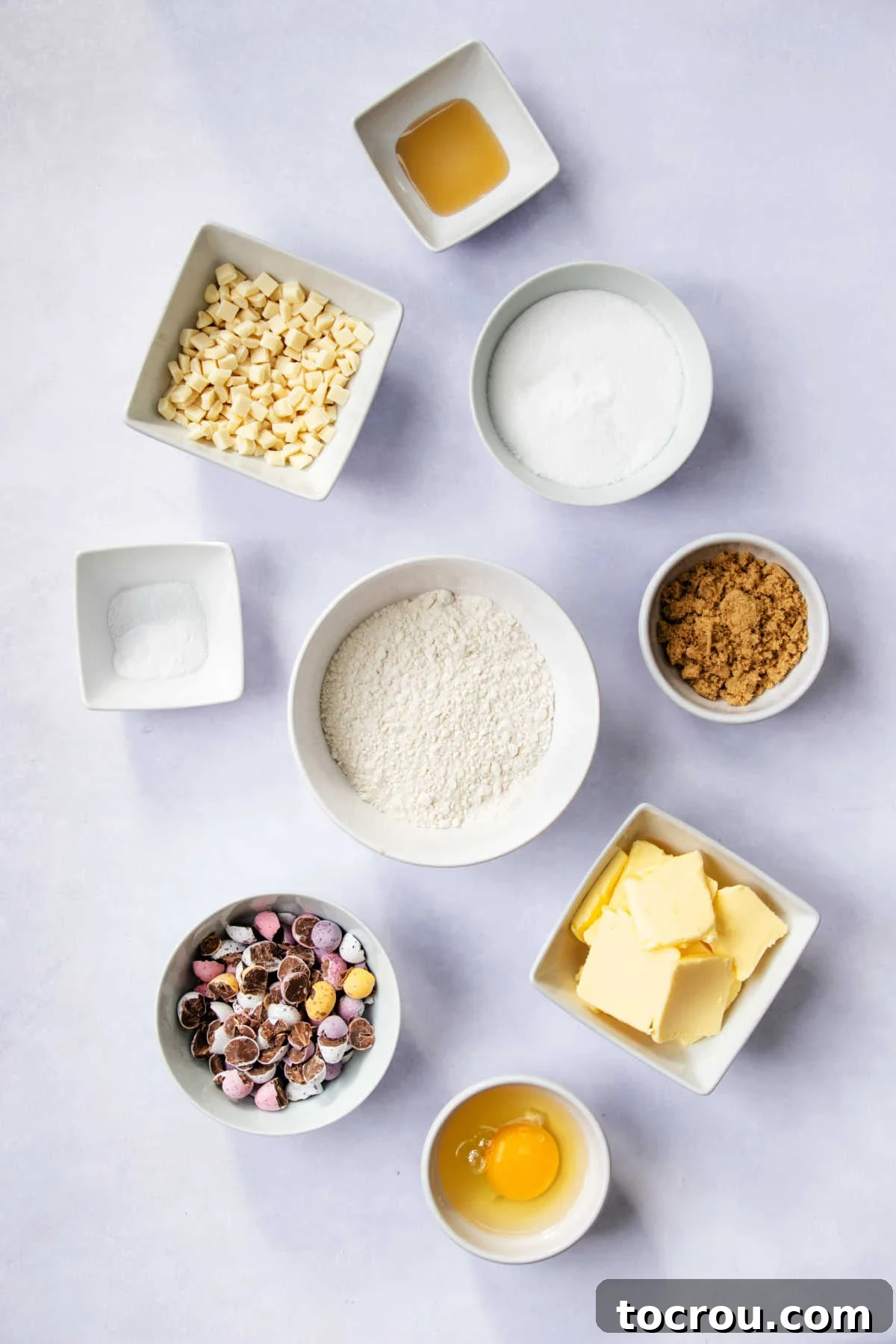 Bowls of essential cookie ingredients including flour, sugars, and butter, neatly arranged and ready for mixing to create chocolate egg cookies.