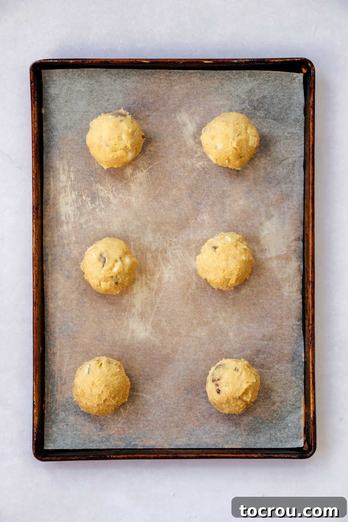 Large, perfectly portioned scoops of cookie dough dotted with Cadbury Mini Eggs and white chocolate, placed on a baking sheet, awaiting their transformation in the oven.