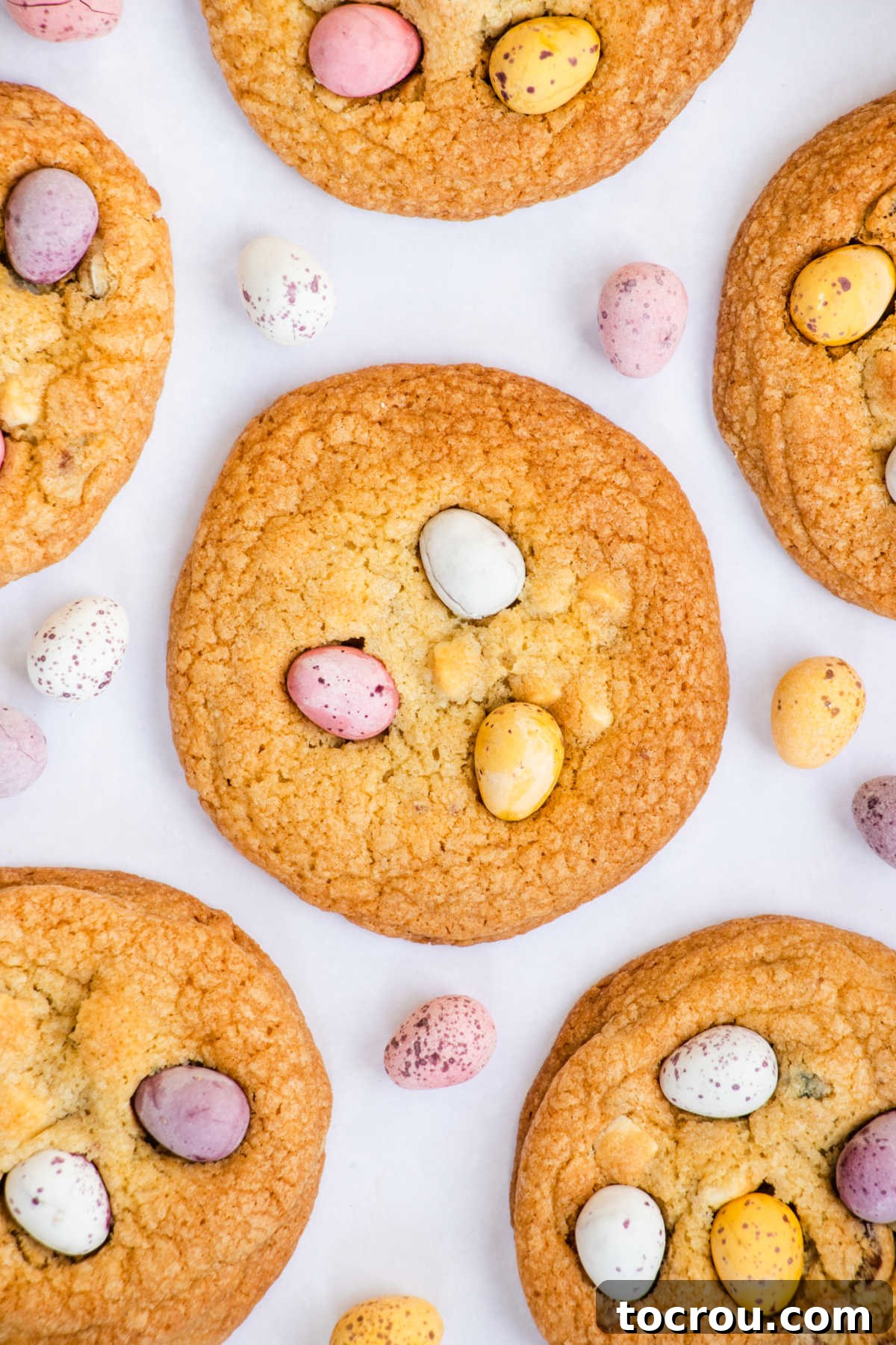 A close-up shot of several large, perfectly baked cookies, generously topped with colorful Cadbury Mini Eggs, highlighting their inviting texture.