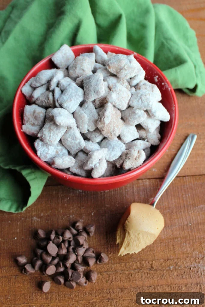 bowl of muddy buddies with a spoonful of peanut butter and pile of chocolate chips.