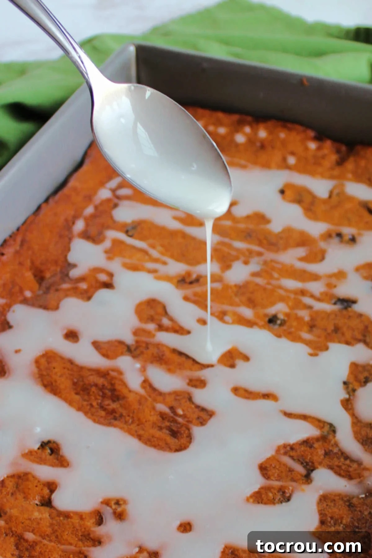 Glazing Poor Man's Cake A spoon delicately drizzling a sweet powdered sugar glaze over a rich, spiced raisin depression cake, creating an appealing finish.