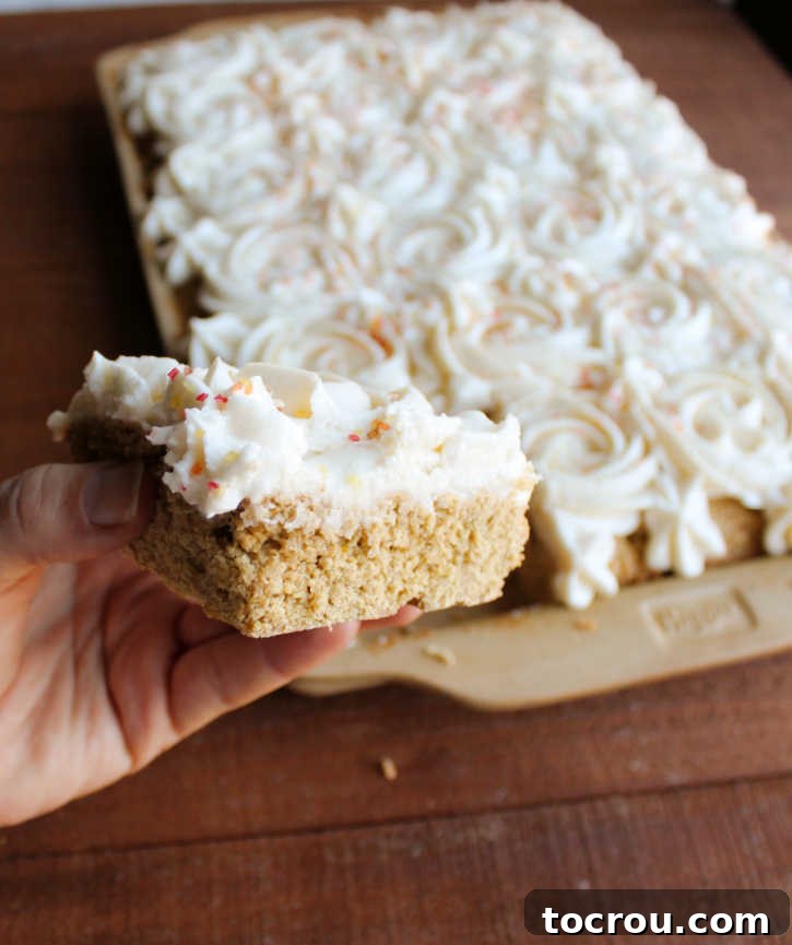 Hand Holding a Pumpkin Spice Cookie Bar A hand holds a square of pumpkin cookie bar, showcasing the perfectly piped frosting rosettes on its surface.