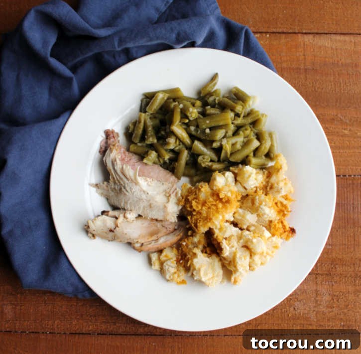 A dinner plate featuring a generous serving of French onion cheesy potato casserole, accompanied by vibrant green beans and slices of grilled turkey, showcasing its versatility as a perfect side dish.