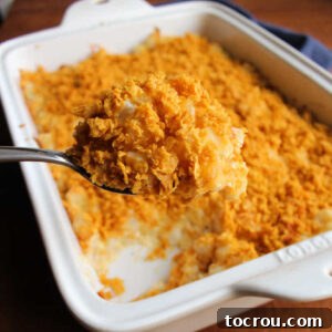 Serving spoon getting a big scoop of French onion cheesy potato casserole topped with golden brown cornflake crumbs.