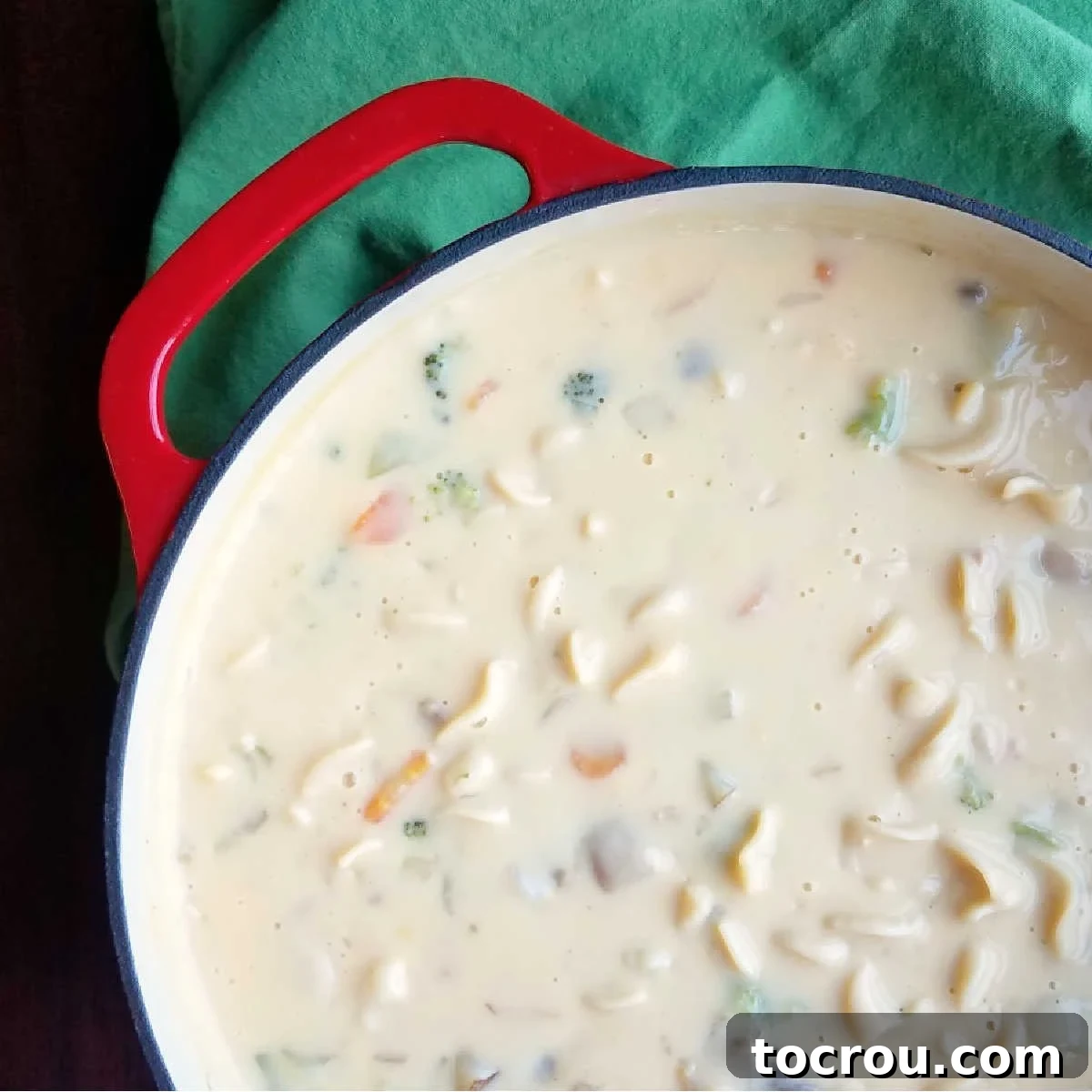 A cast iron Dutch oven overflowing with rich, creamy Kelly's cheese soup, featuring visible chunks of vegetables and pasta, ready to be served.