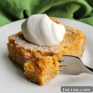 Fork going into piece of pumpkin gooey butter cake topped with maple whipped cream.
