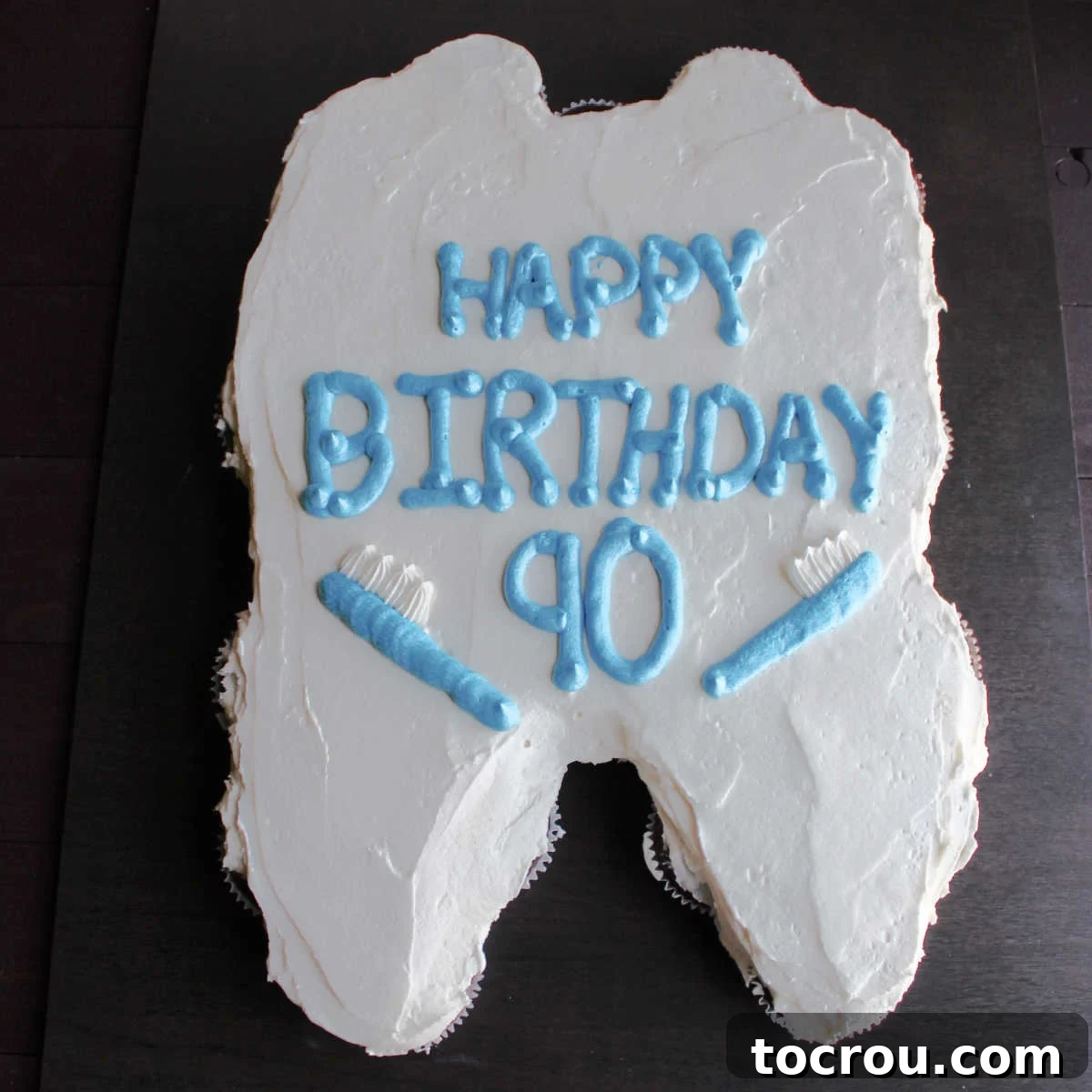 A cute tooth-shaped cupcake pull-apart cake decorated with 'Happy Birthday' and frosting toothbrushes.