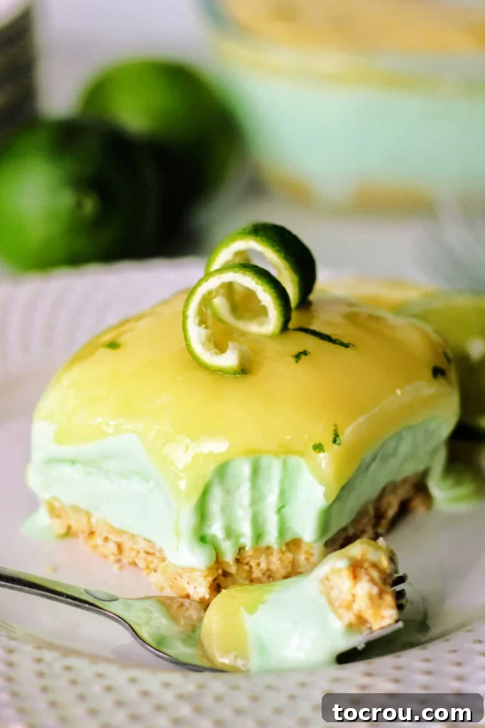 bite of layered lime sherbet bar on fork showing cracker crust, creamy sherbet center and bright lime curd topping.