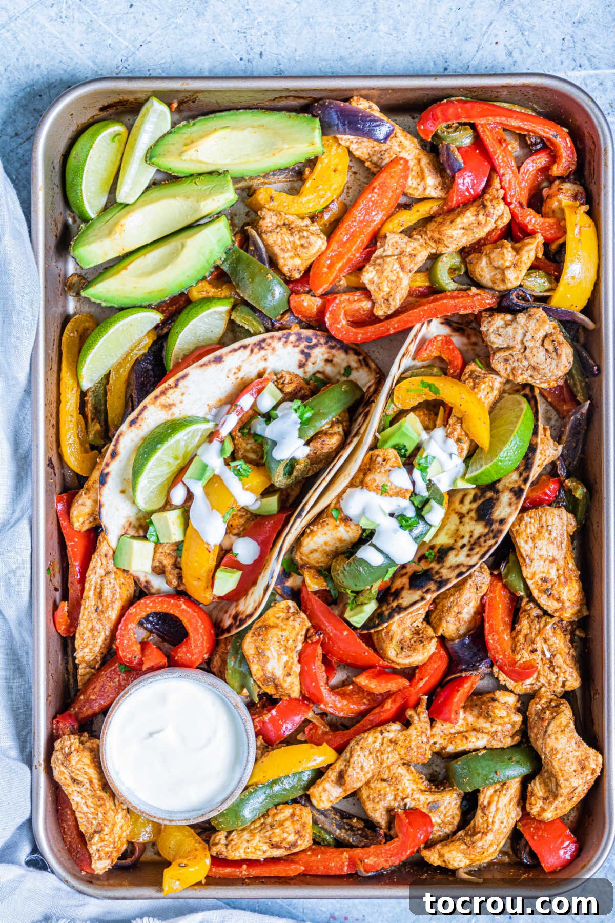 One-Pan Chicken Fajitas 4 Sheet pan filled with chicken fajita fixings with avocado wedges, limes and sour cream.