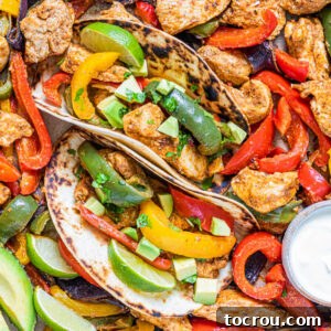 One-Pan Chicken Fajitas 8 Close up of chicken fajitas with colorful pepper slices and onions with seasoned chicken in toasted tortillas with lime wedges and sour cream.