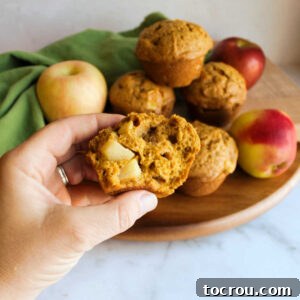 hand holding half a pumpkin muffin with chunks of apple inside.