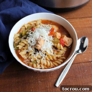 A bowl of Slow Cooker Chicken Tomato Soup topped with fresh herbs and a generous sprinkle of shredded cheese.