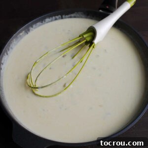 Skillet filled with sour cream and cheese sauce with bits of chopped green chilies.