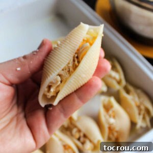 Hand holding jumbo stuffed shell filled with shredded chicken and cheese.