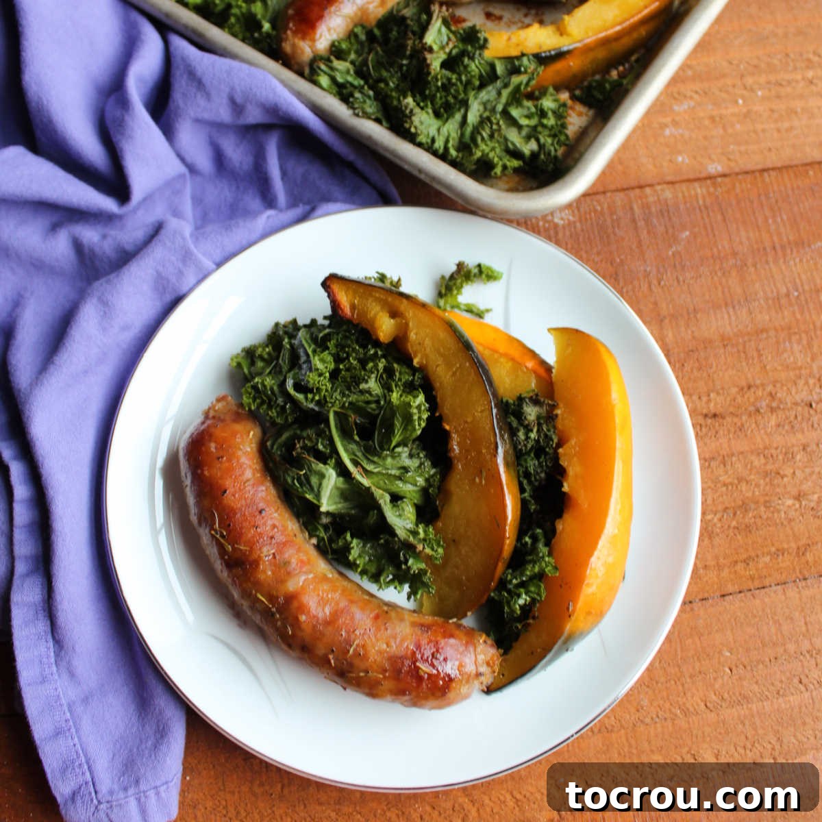 A beautifully arranged plate of roasted Italian sausage, tender acorn squash, and crispy kale, ready to be enjoyed.