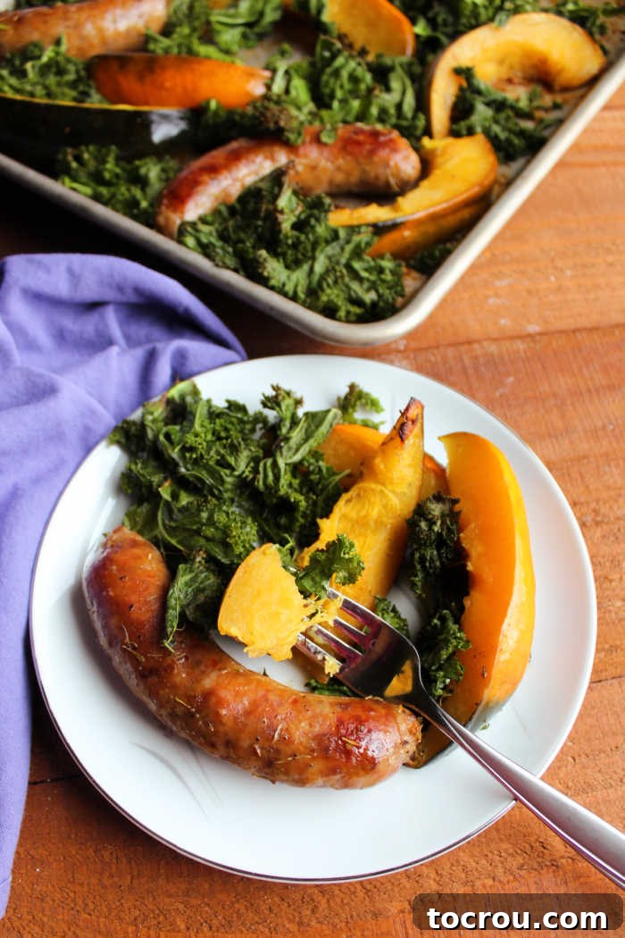 A close-up shot of a fork holding a perfectly tender piece of acorn squash, with a plate of roasted kale and Italian sausage blurred in the background, highlighting the succulence of the squash.