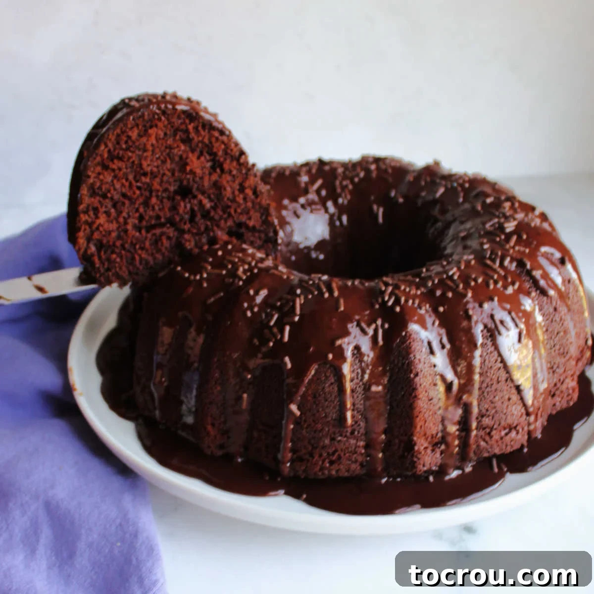 Lifting first slice of moist chocolate bundt cake out of cake.