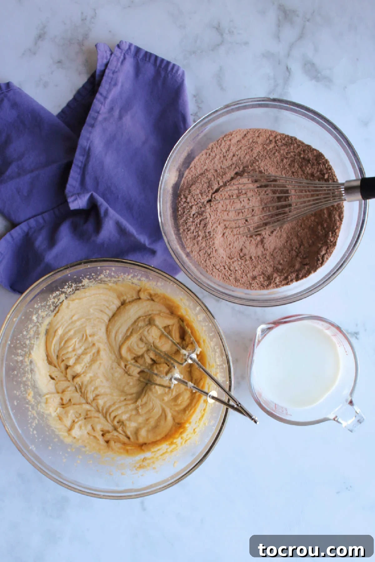 Bowl of creamed butter and sugars, bowl of flour and cocoa powder mixture and measuring cup of milk.