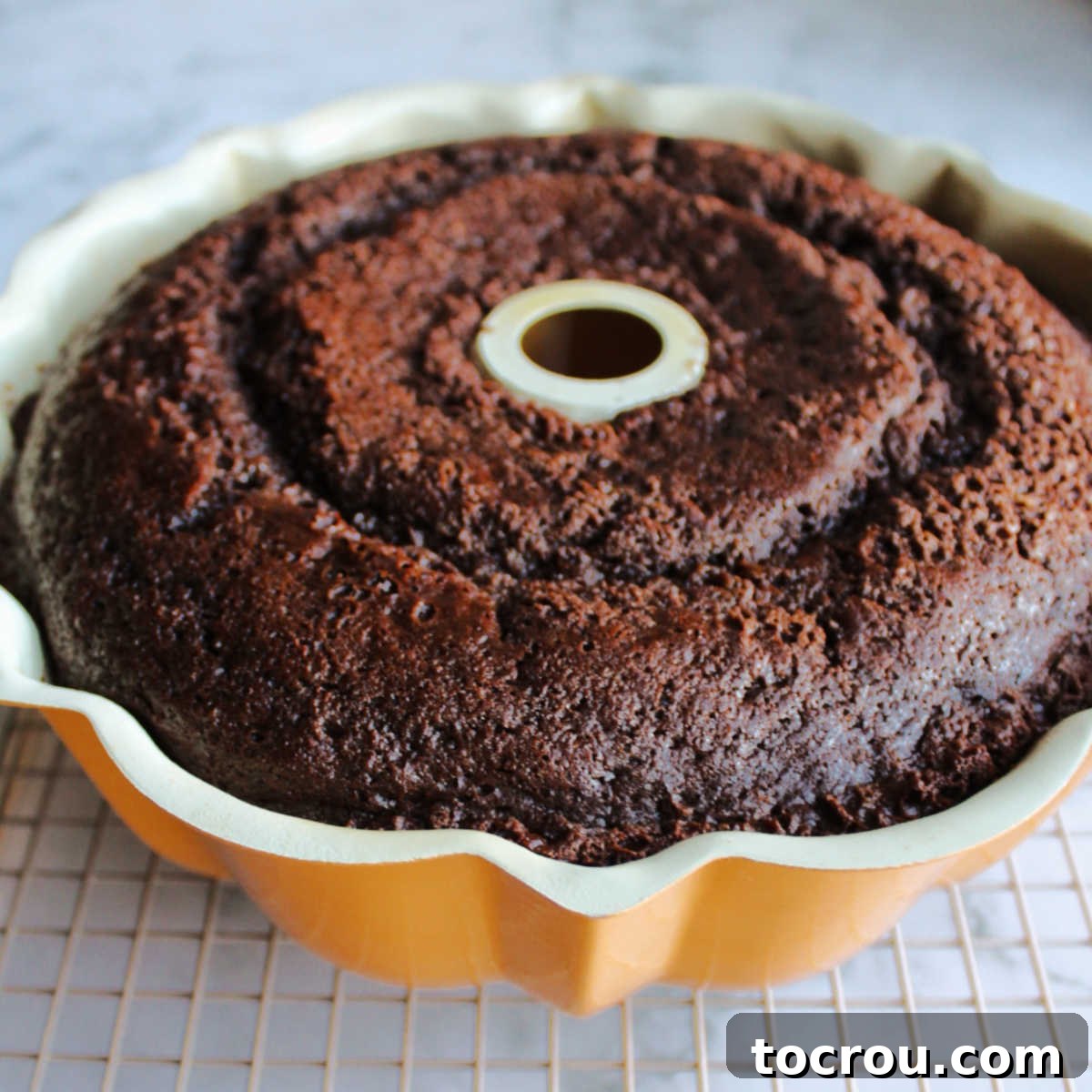 Freshly baked chocolate cake in bundt pan cooling on wire rack.