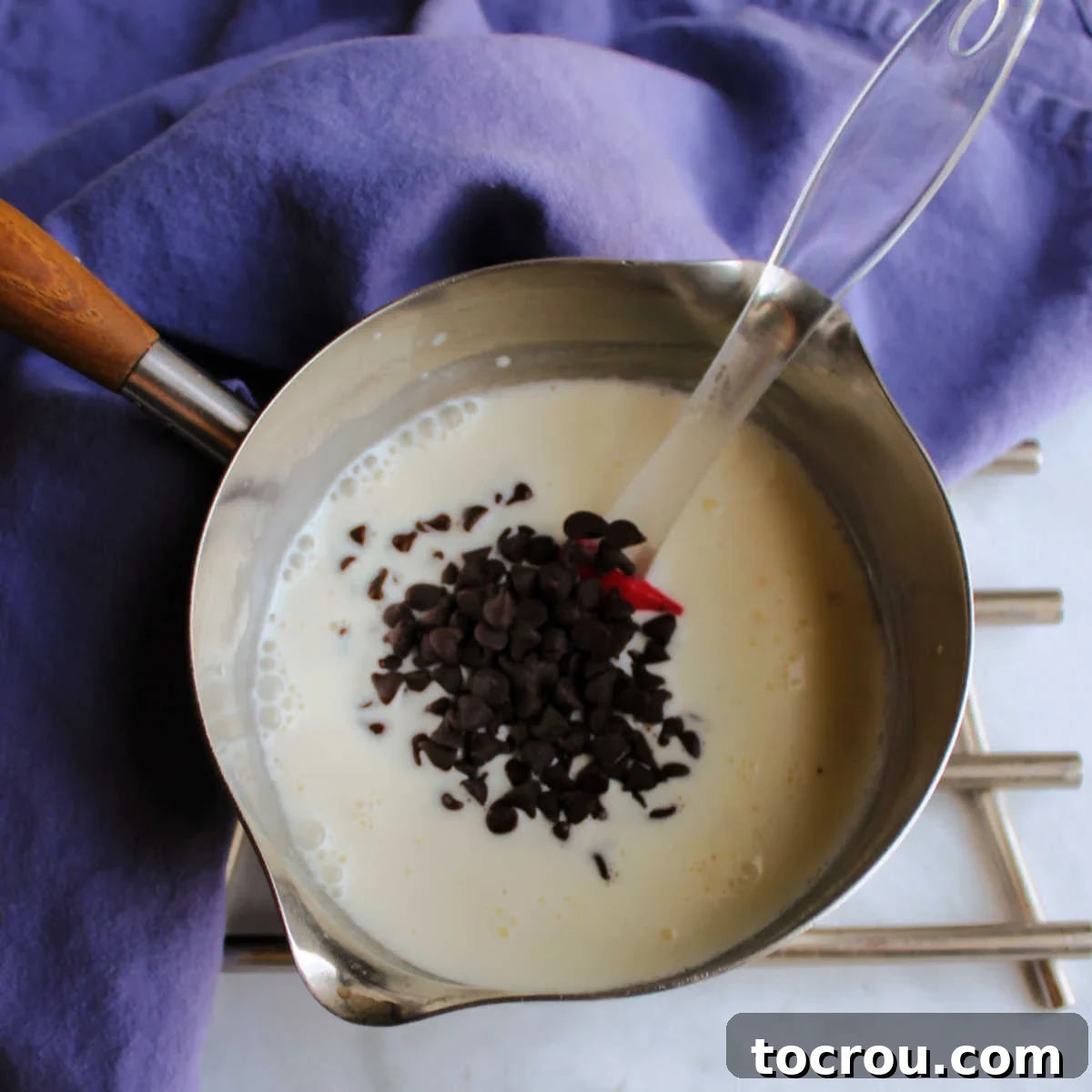 Chocolate chips melting in warm cream in sauce pan.