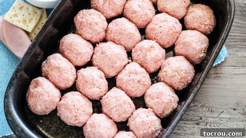 Pan filled with uniform, pink raw ham balls, perfectly shaped and ready to be baked in the oven.