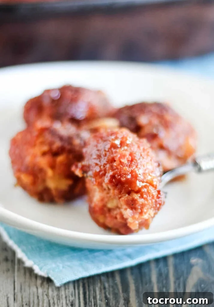 Fork full of a glazed ham ball, showing the tender interior and sticky glaze, ready to be eaten.