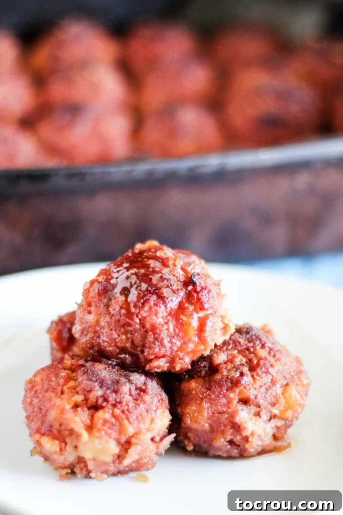 Stack of perfectly glazed ham balls on a white plate, glistening with their sweet and savory coating.