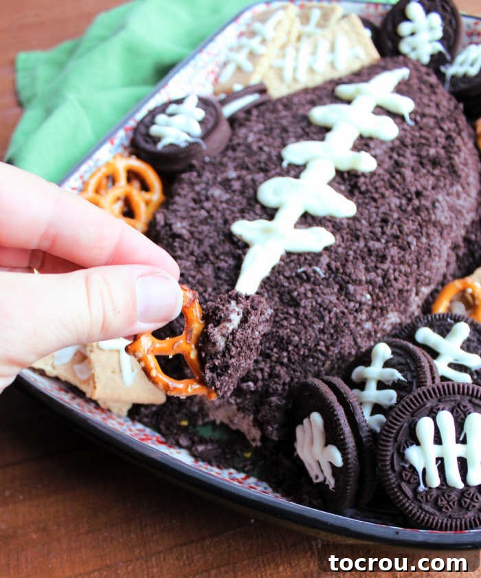 Dipping pretzel into football shaped chocolate cheese ball, showcasing the rich texture.