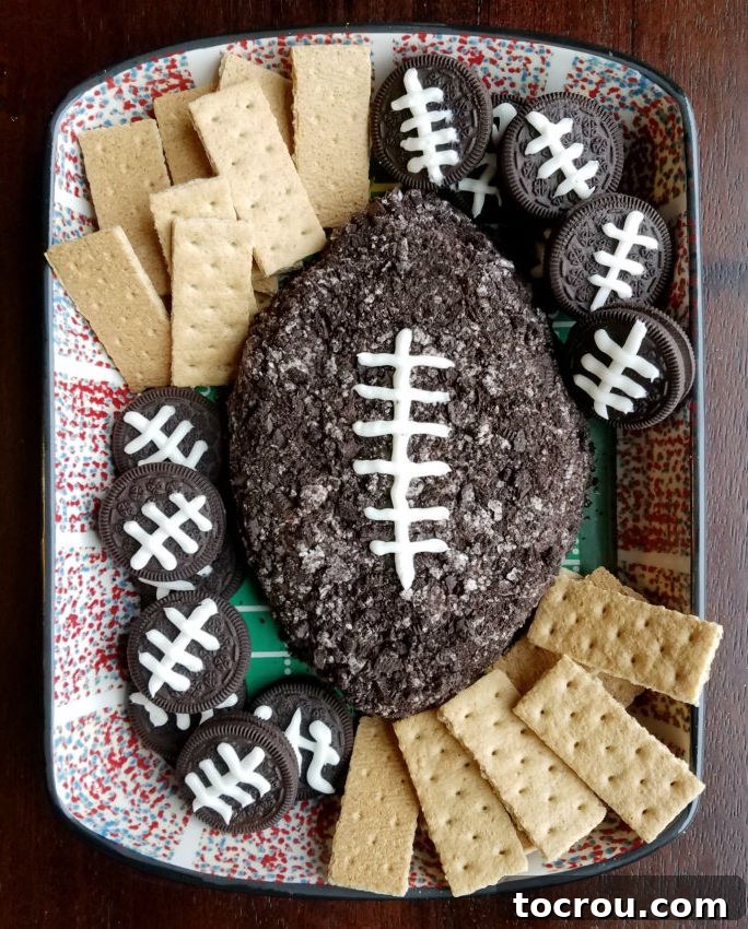 Serving dish with Oreo cheeseball shaped like a football served with Oreos with football laces and graham crackers.
