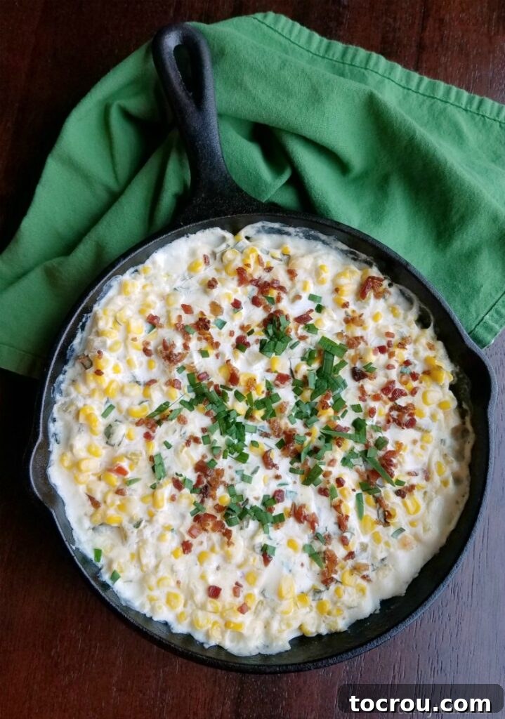 Ultimate Cheesy Corn Dip 5 A warm cast iron skillet filled with creamy corn dip, beautifully garnished with crispy bacon, fresh cilantro, and vibrant chives, ready to be served.
