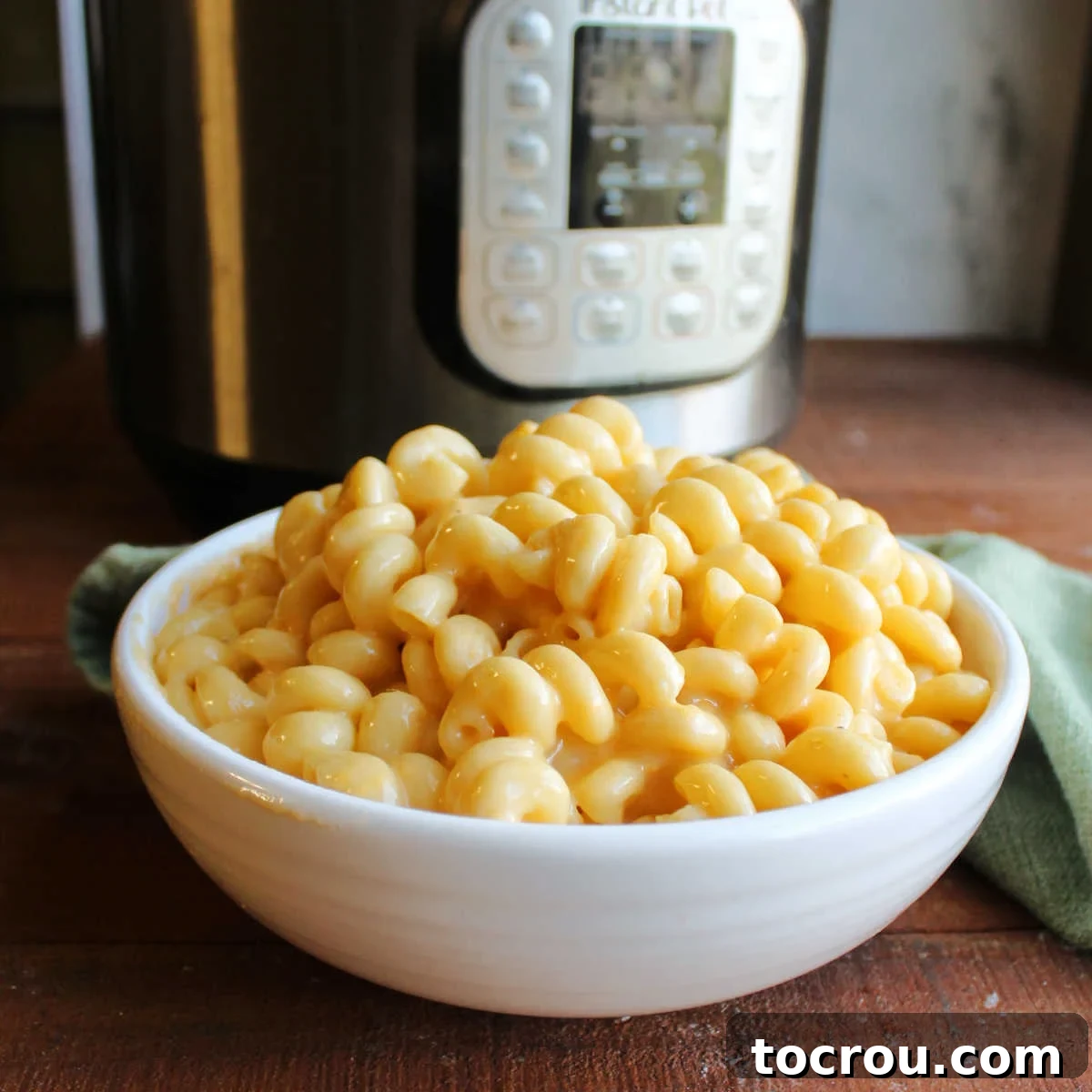 Bowl of creamy curly mac and cheese in front of instant pot.