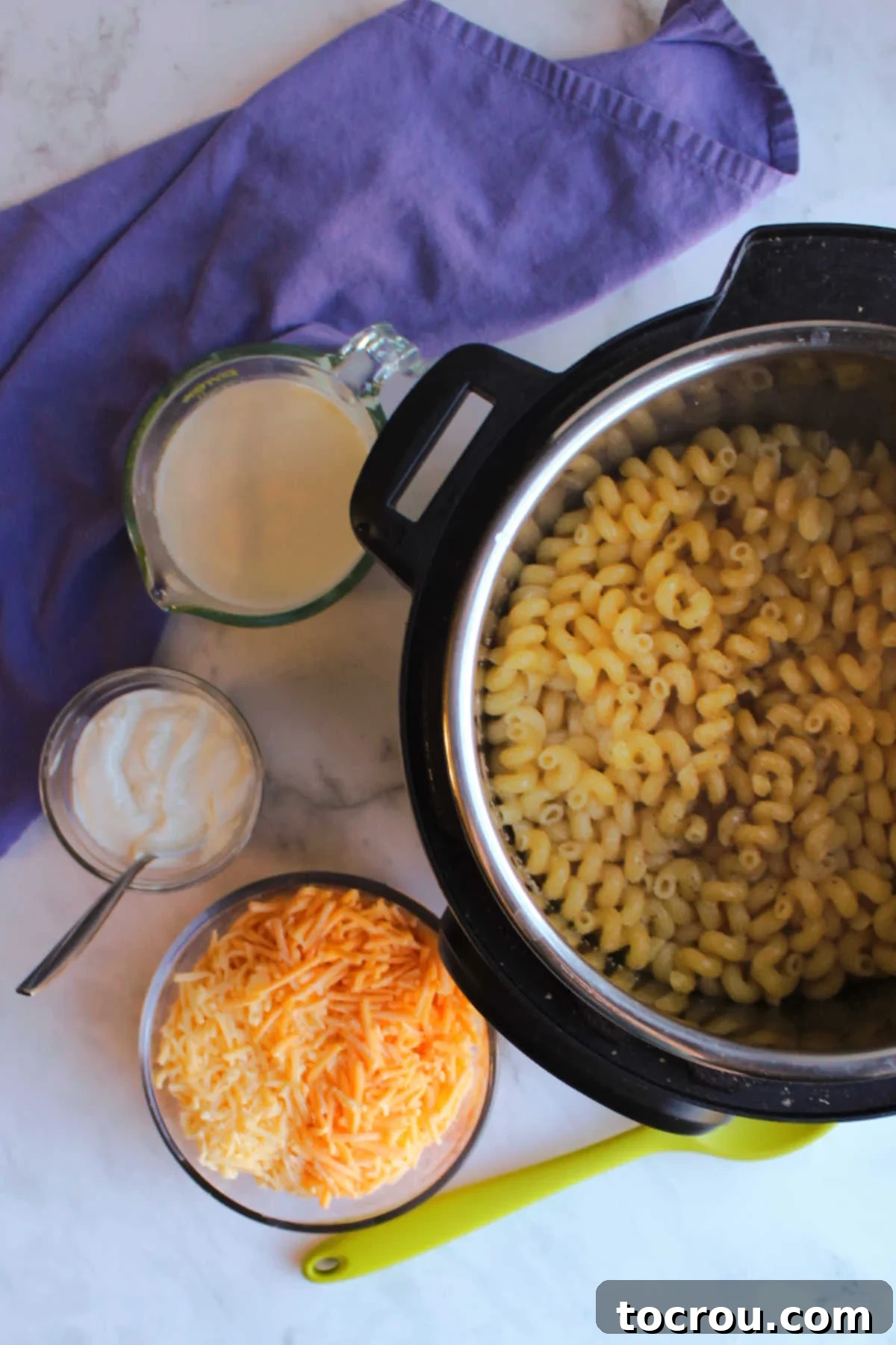 Instant pot filled with water and pasta next to bowls of cheese, sour cream and milk.