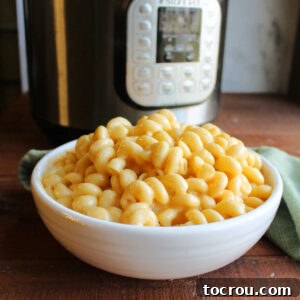 Bowl of creamy curly mac and cheese in front of instant pot.