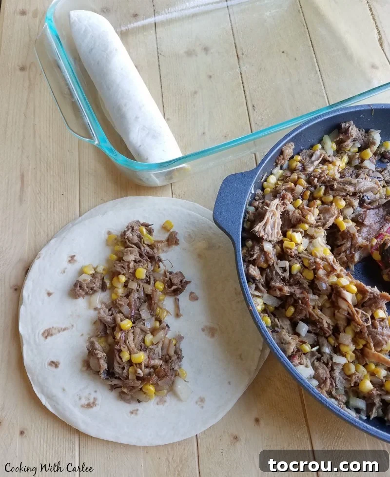 Skillet filled with a mixture of BBQ pulled pork and corn, being scooped onto tortillas to be rolled into enchiladas.