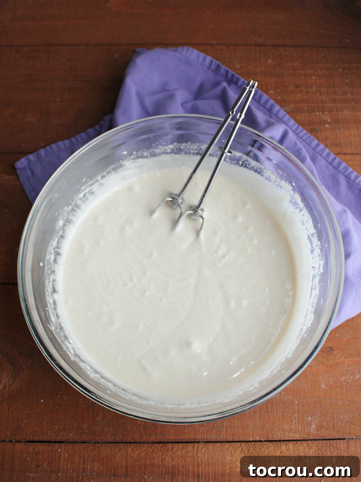 Thick, creamy white cupcake batter, enhanced with sour cream, flour, and sugar, prepared in a mixing bowl for a superior semi-homemade cupcake. Mixing bowl with semi-homemade white cupcake batter inside that started with a cake mix but added sour cream, flour, sugar and more to make a thick white batter.