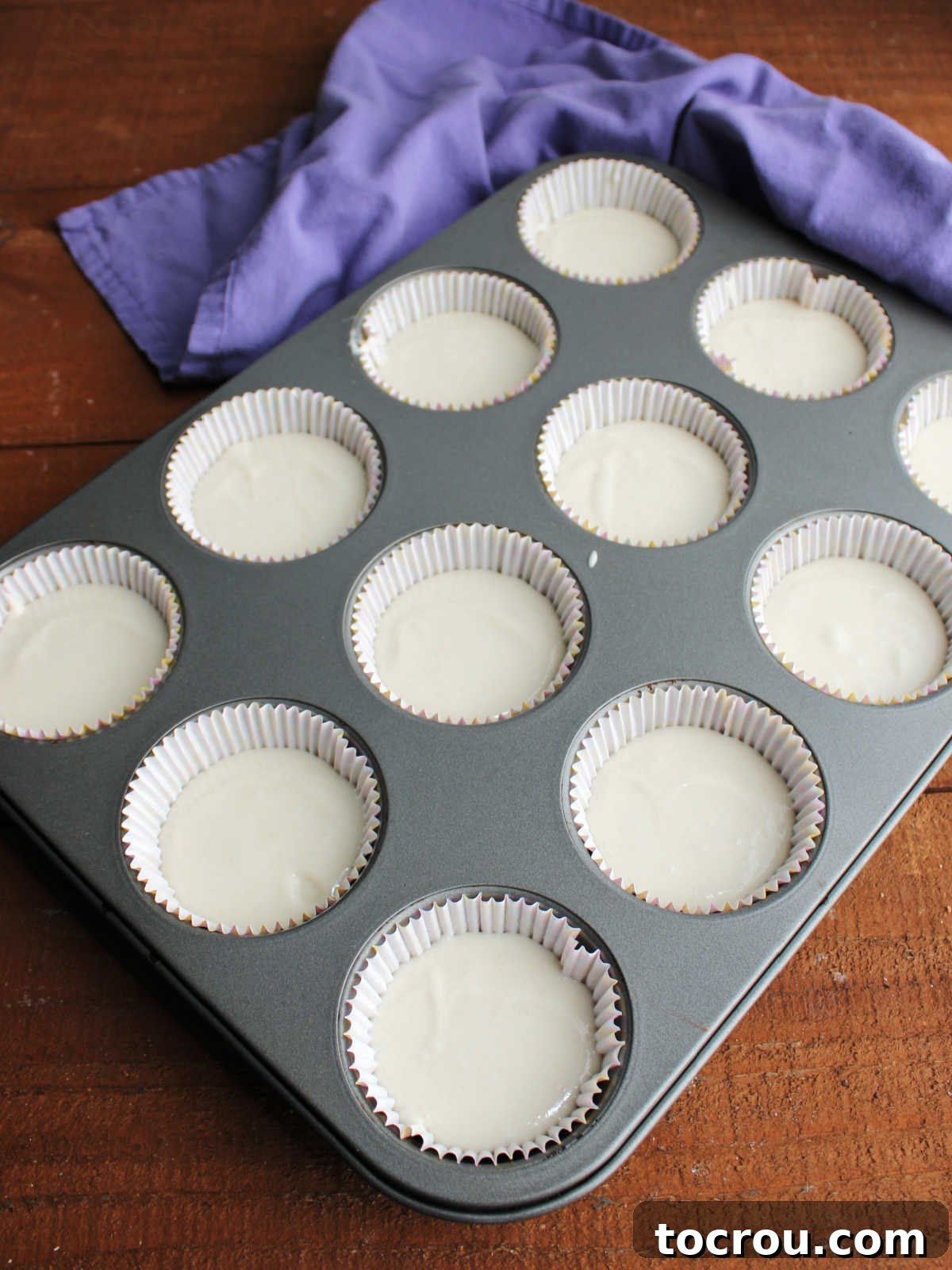 Cupcake liners filled with smooth, white batter, poised for baking into fluffy treats. White cupcake batter perfectly scooped into paper liners, filling each well about two-thirds full, ready for baking.