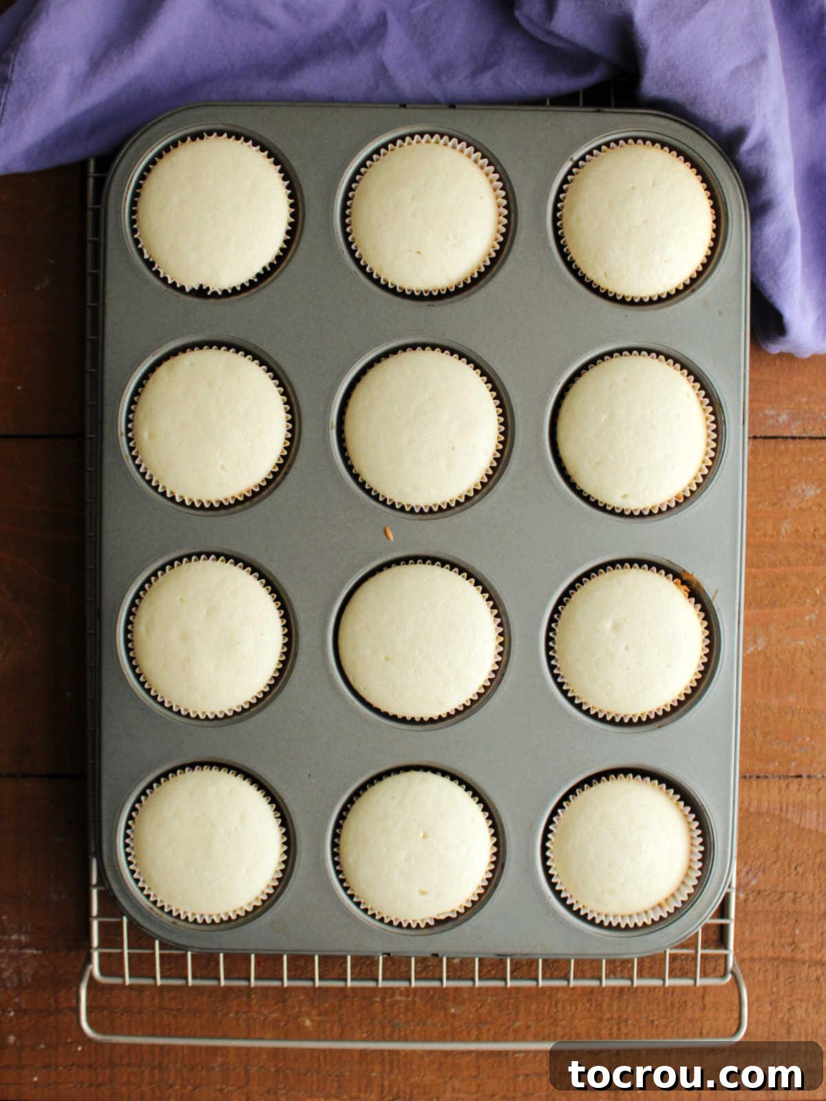 Muffin tray showcasing a batch of pale, perfectly baked white cupcakes, ready to be cooled and decorated. Muffin tray filled with freshly baked white cupcakes that still have a very pale appearance and almost no browning.