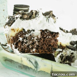 Lifting a perfect piece of Oreo cheesecake poke cake out of the baking pan, showcasing its moist layers of cake, rich pudding, and creamy topping.